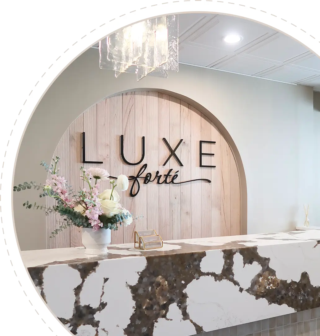 Reception desk with marble counter, flower arrangement, and 'LUXE forté' sign on wooden panel wall.